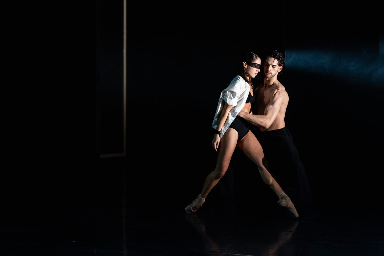 Scene from Don Juan by Robert Bondara: a woman in a blindfold and an open white shirt and a shirtless man dance a duet in a pool of light on a dark stage