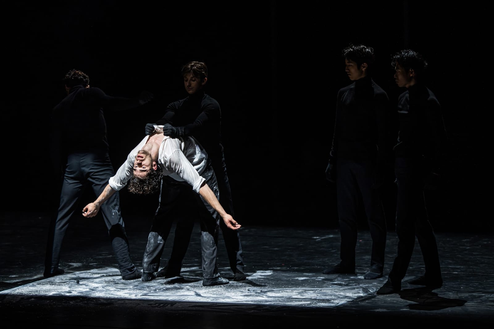 Scene from Don Juan by Robert Bondara: a dancer in a white shirt bent backwards, held by a dancer in black, with three more dancers in black standing in a spotlight of white powder