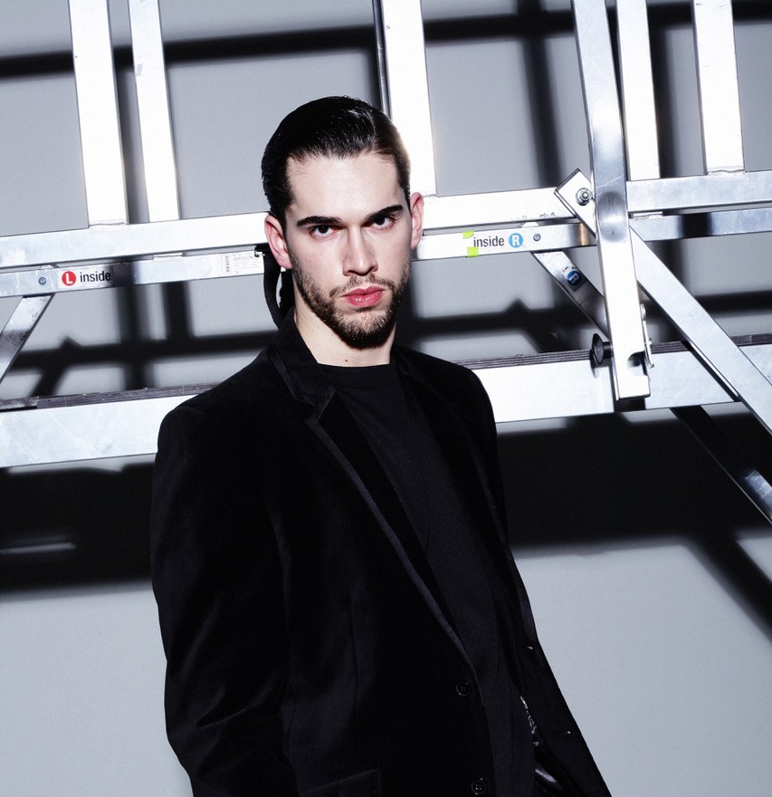 Alexandre Sellani in a black suit, portrait against a scaffolding set