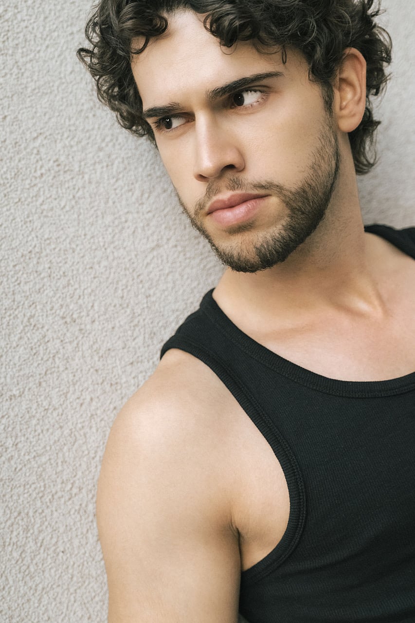 Alexandre Sellani in a black tank top, glancing sideways against a textured wall